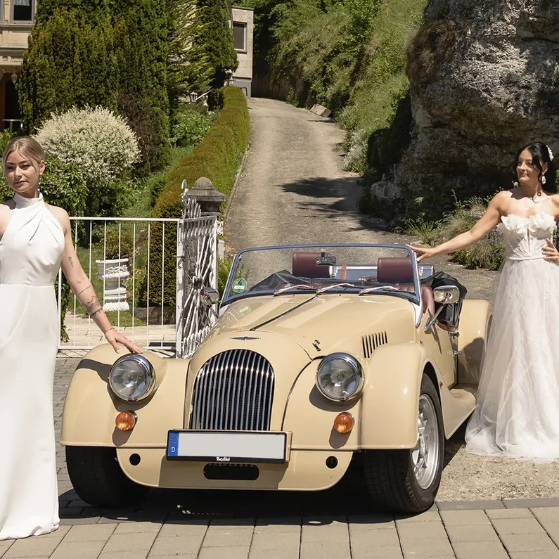 Weibliches Brautpaar mit Morgan Roadster vor SchlossFUN Seeburg